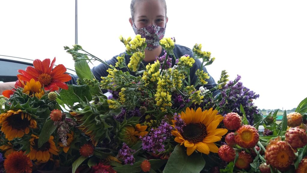 Liz Rohricht ‘21, masked, stands in front of an assortment of flowers.